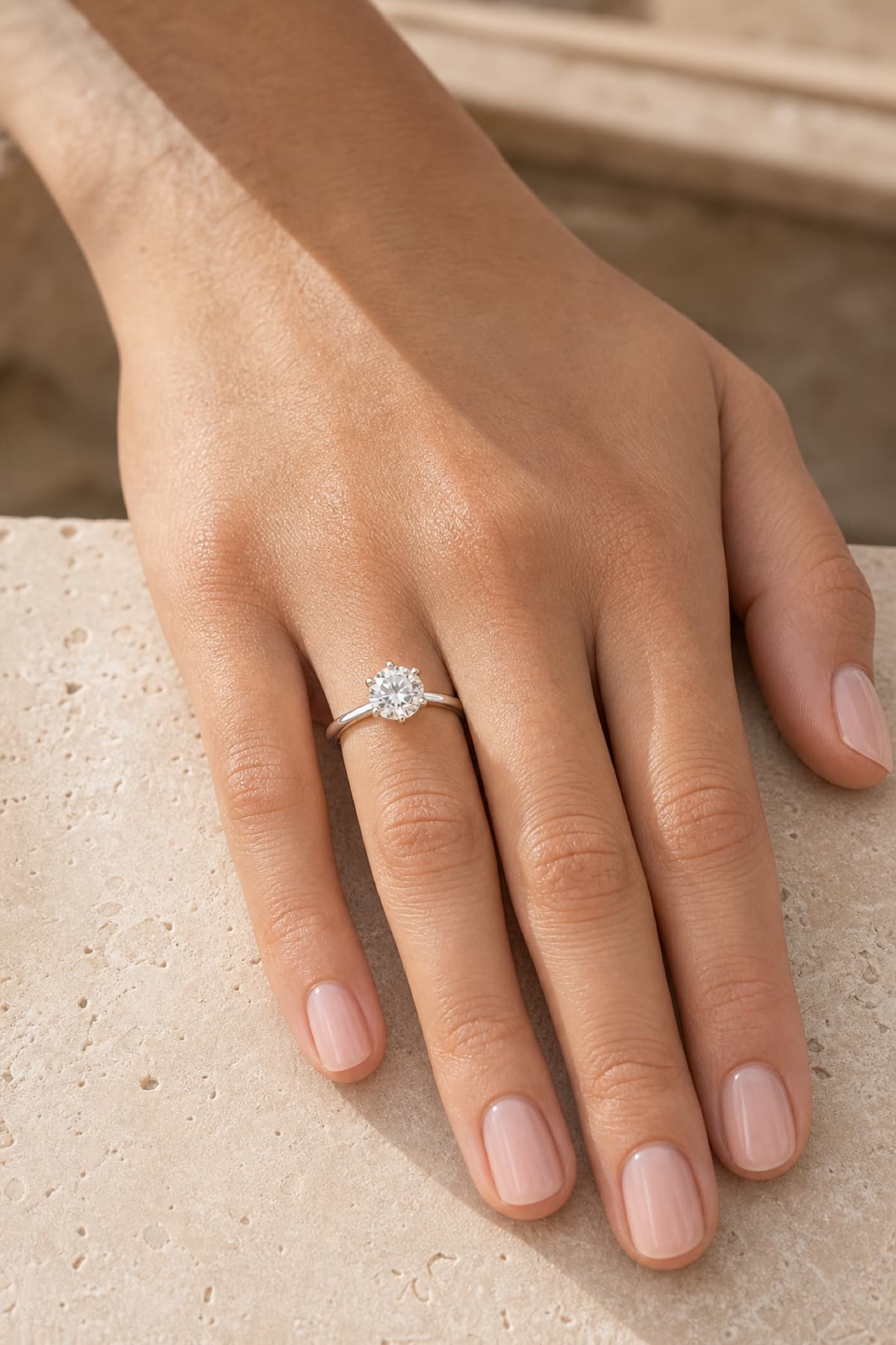 Classic round solitaire engagement ring on a woman's left hand ring finger in a warm jeweler's studio