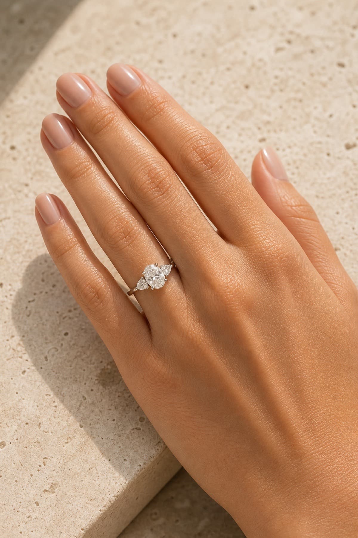Three-stone engagement ring on a woman's left hand ring finger in a warm jeweler's studio