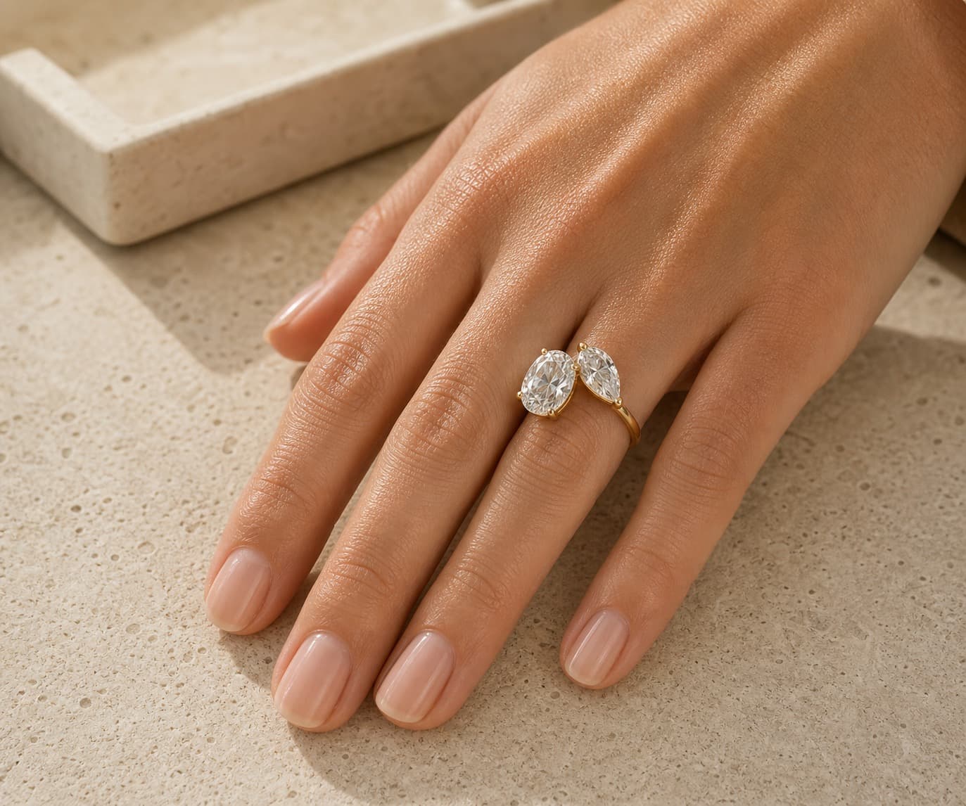 Toi et Moi two-stone engagement ring on a woman's left hand ring finger in a warm private jeweler's studio